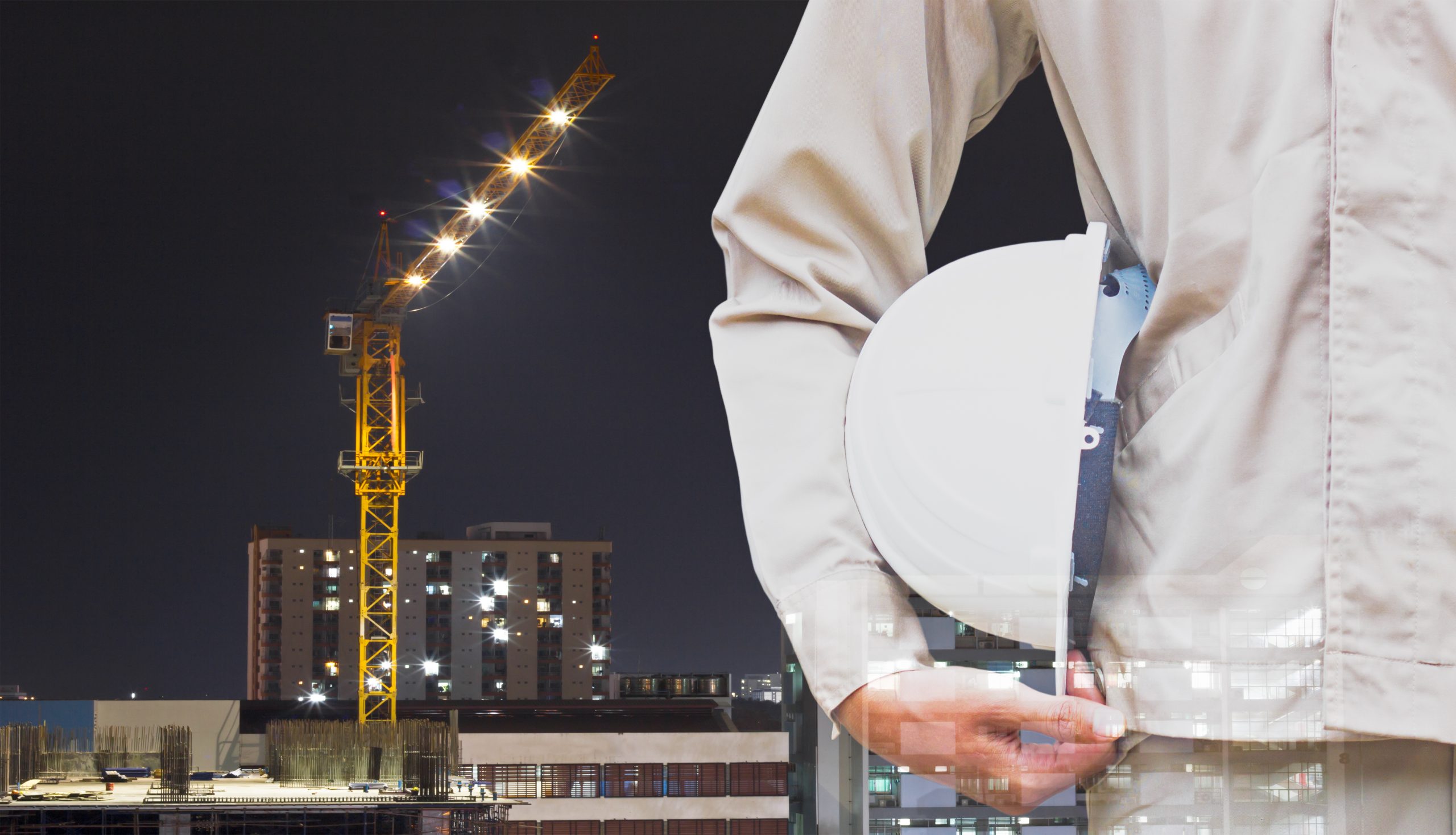 man holding construction hat on hip in front of a construction crane