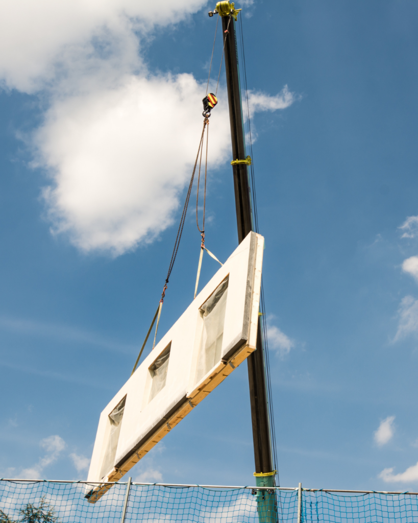 A prefabricated wall being lifted onto a jobsite by a forklift. 