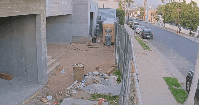 A man sneaking under a fence at a construction site captured by a TrueLook security camera