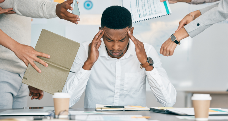 Man sitting at a conference room table with a notebook open and multiple people stressing him out by handing him a journal, showing him a phone, showing him a report, and the time
