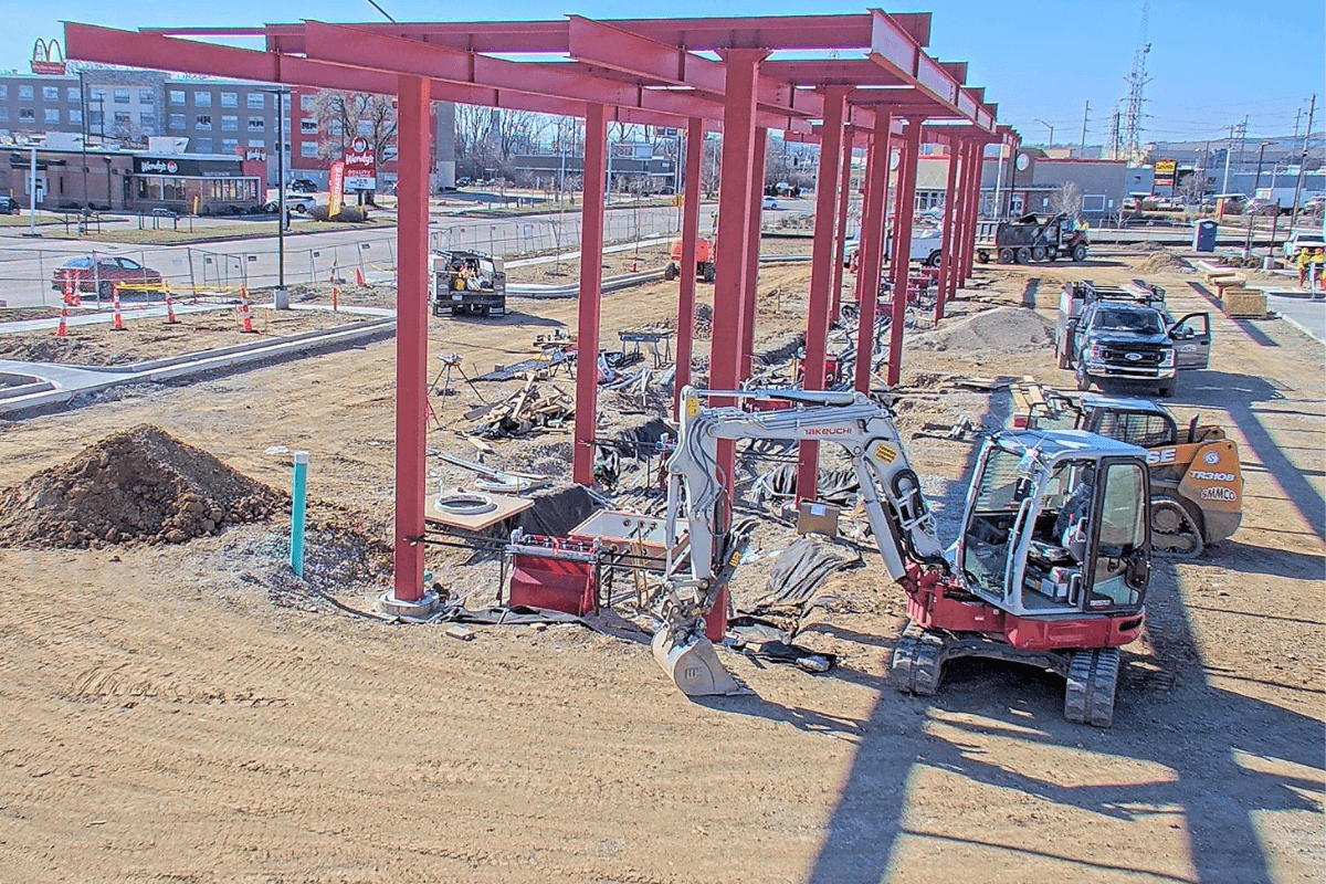 Excavator working beside a red steel canopy frame on a QuikTrip construction site