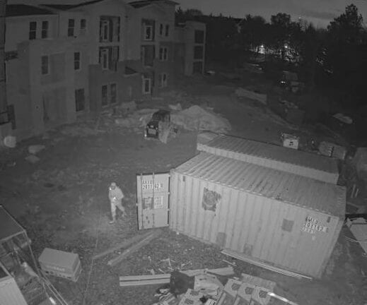 Infrared night vision camera view showing a person near a shipping container on a jobsite