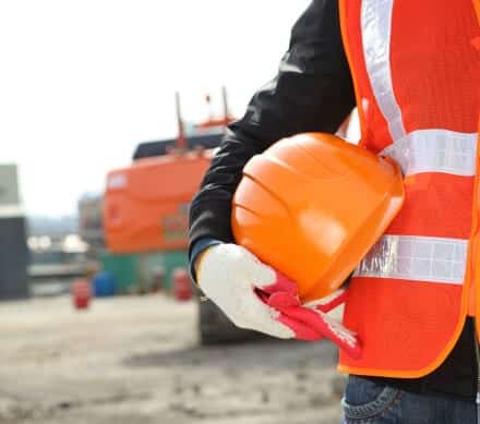 Worker in a safety vest holding an orange hard hat