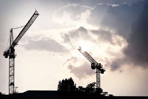 Tower cranes silhouetted against a cloudy sky