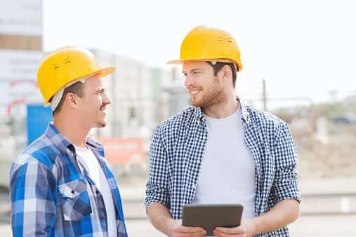 Two smiling construction workers in hard hats with a tablet