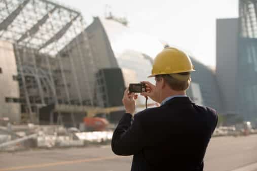 Man in a hard hat photographing a building with a small camera