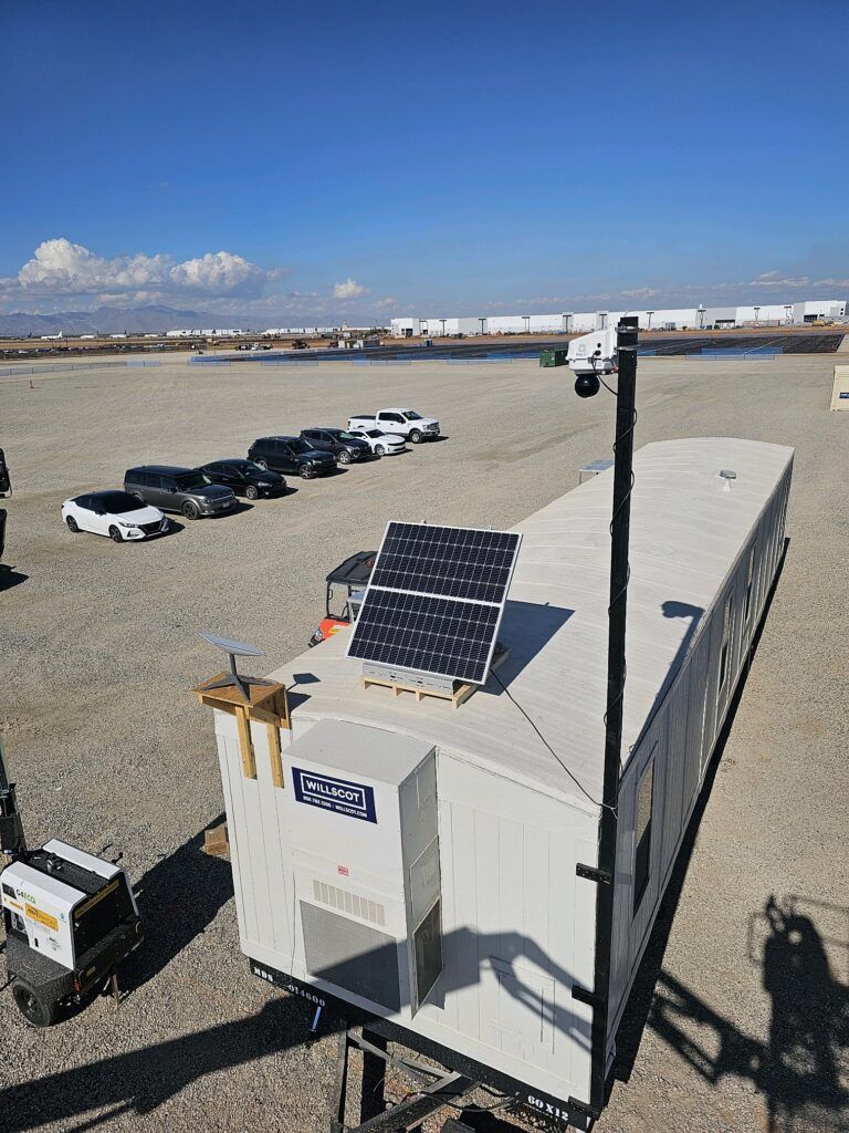 Solar-powered pan-tilt-zoom camera mounted on a pole beside a jobsite trailer