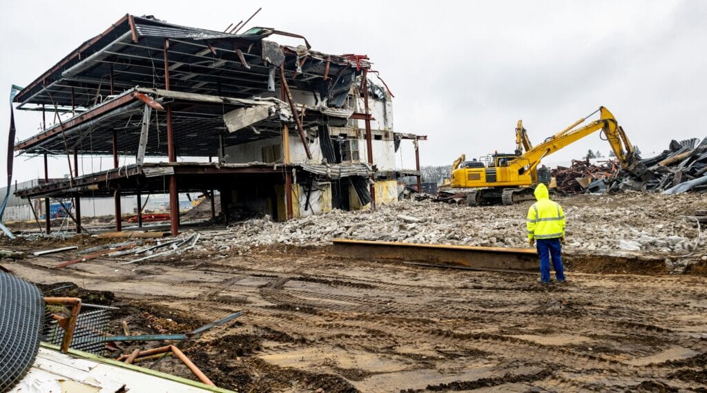 Construction demolition occurring with a CAT machine and a worker in PPE