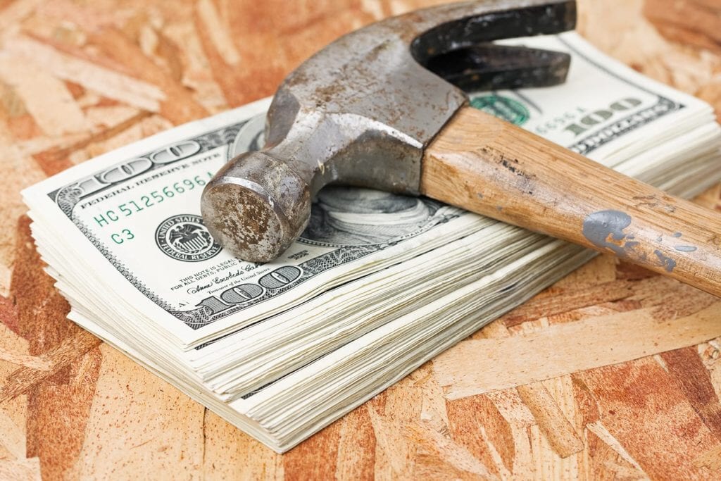 A pile of cash with a $100 bill showing and a hammer lying on top of it