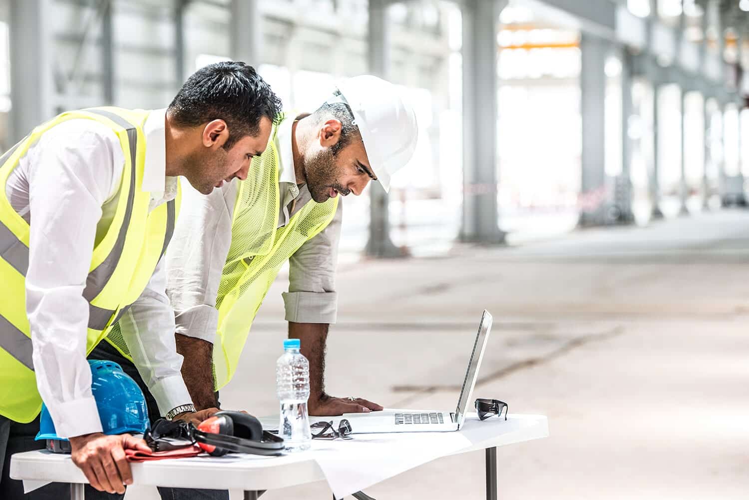 Two engineers in hard hats reviewing a laptop