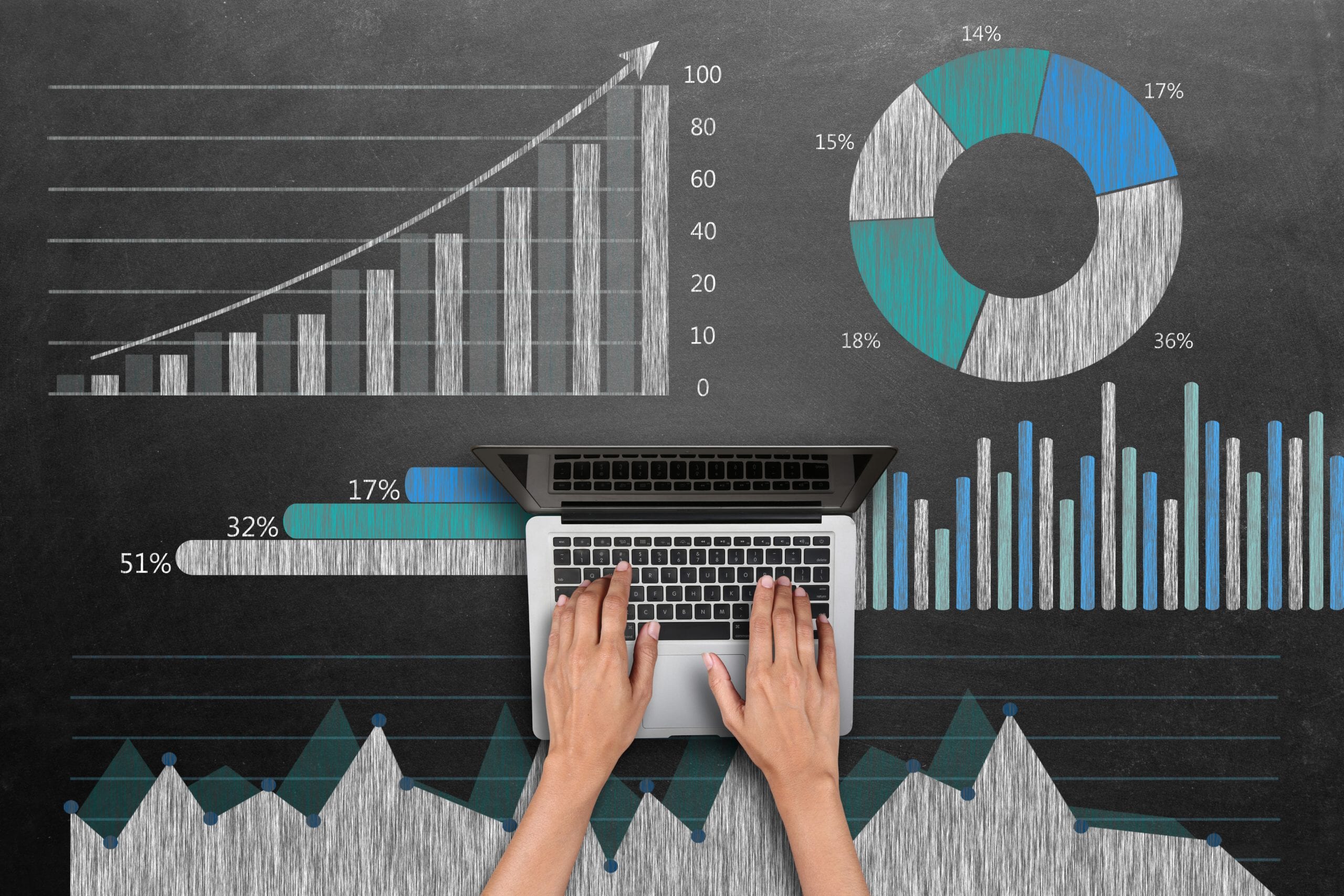 Hands typing on a laptop over chalkboard charts