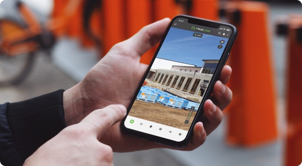 Hand holding a phone showing a live TrueLook camera view of a jobsite