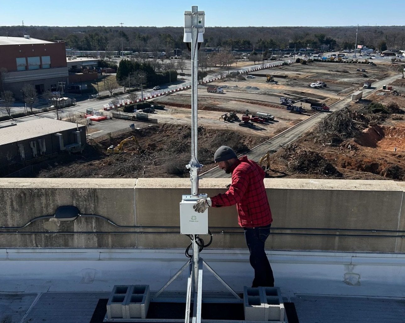 Installer adjusting a TrueLook camera on a non-penetrating rooftop mount above a jobsite