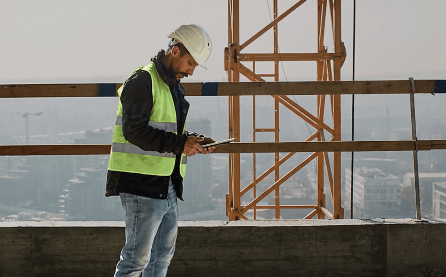 Construction project manager in a hard hat checking a tablet on a jobsite
