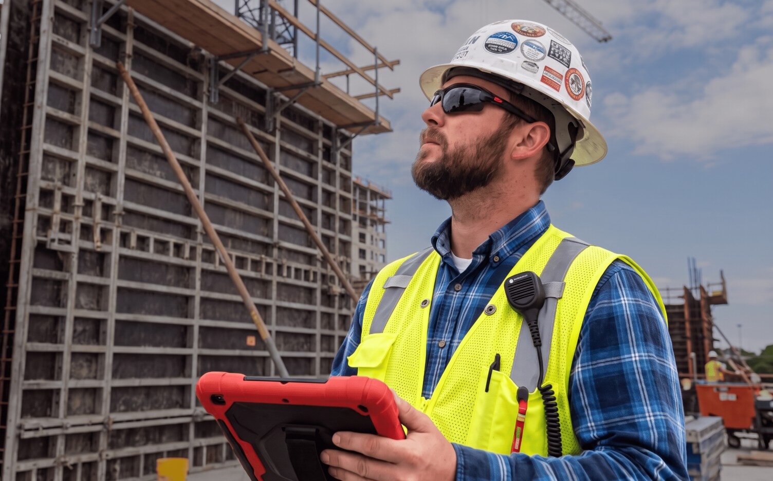 Safety manager in a hard hat and hi-vis vest holding a tablet on a jobsite